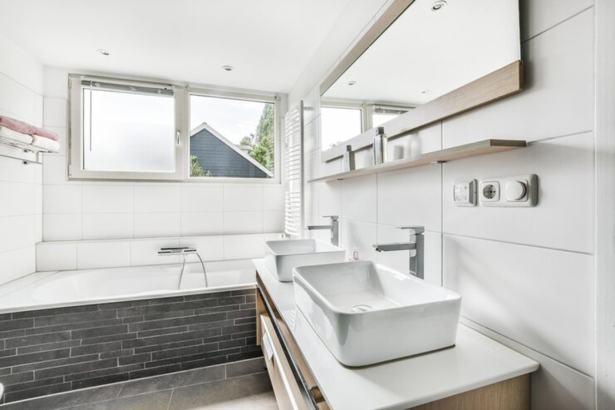Modern bathroom featuring a sleek bathtub, two washbasins, wooden shelves, and large windows for natural light